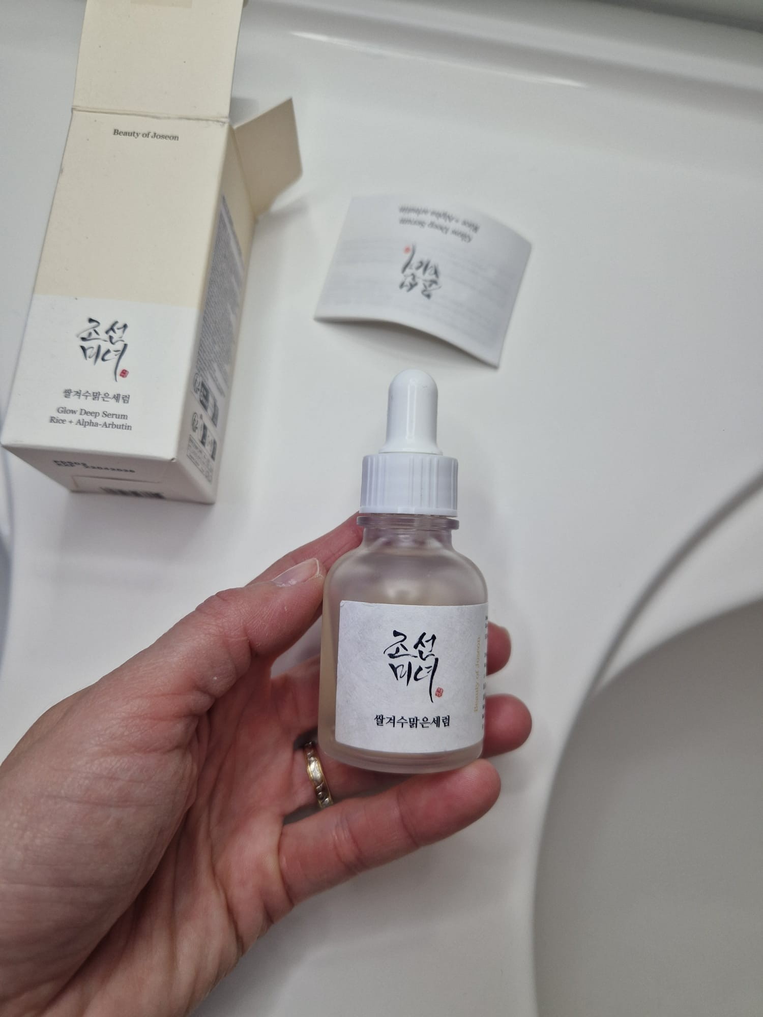 Beauty of Joseon Glow Deep Serum tenu à la main avec sa boîte ouverte et sa notice en arrière-plan.
