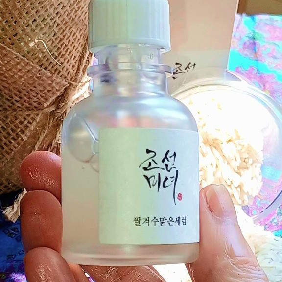 Flacon Beauty of Joseon Glow Deep Serum tenu à la main devant un récipient contenant du riz.