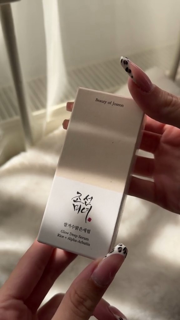 Boîte du Beauty of Joseon Glow Deep Serum Rice + Alpha-Arbutin tenue à la main près d’une fenêtre.