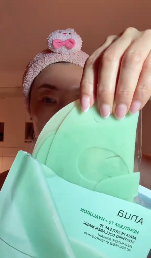 Femme portant un masque Anua Heartleaf 70 + Hyaluron et tenant le sachet du produit devant elle.