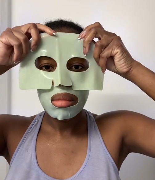 Femme à la peau foncée ajustant la partie supérieure de l’Anua Heartleaf 70 + Hyaluron Soothing Collagen Mask sur son visage.