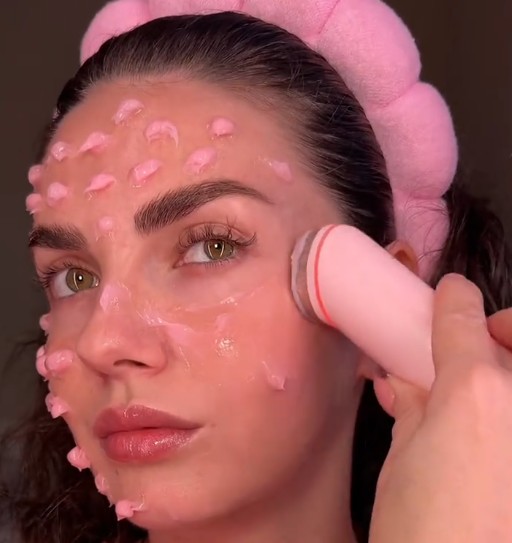 Femme appliquant le Medicube AGE-R Booster Pro Pink Edition sur la joue après avoir réparti un soin sur le visage.