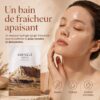 Femme à la peau lumineuse aux côtés du SKIN1004 Madagascar Centella Watergel Sheet Ampoule Mask, illustrant un bain de fraîcheur apaisant.