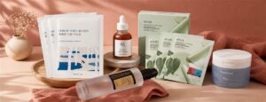 Sélection de produits coréens K-beauty pour peau mature — ROUNDLAB, Beauty of Joseon, Anua, COSRX disposés sur fond terracotta doux