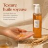Texture fluide et soyeuse du Ginseng Cleansing Oil de Beauty of Joseon versée dans la main, avec le flacon et des racines de ginseng.