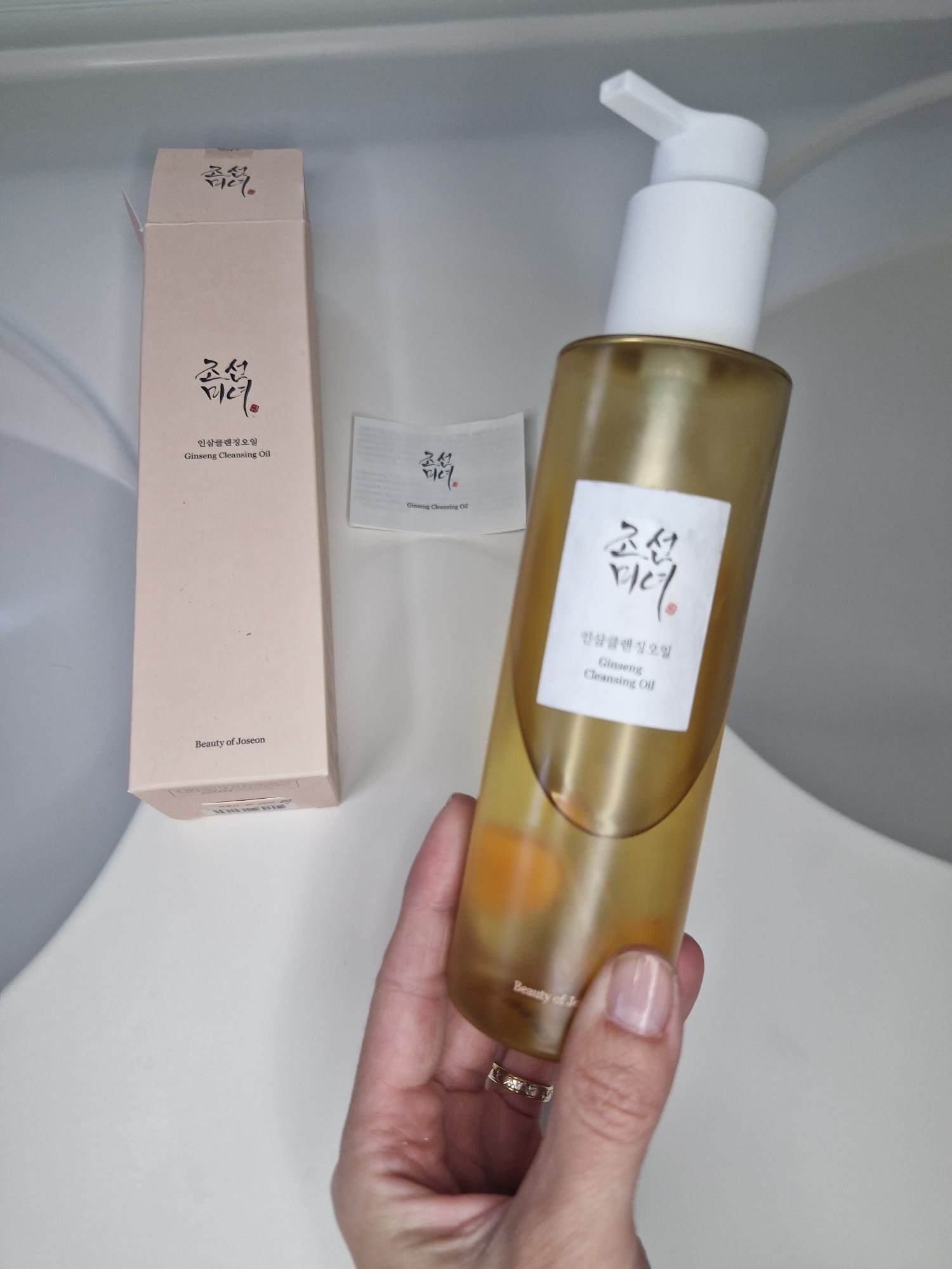 Beauty of Joseon Ginseng Cleansing Oil présenté en main avec sa boîte et sa notice à côté.