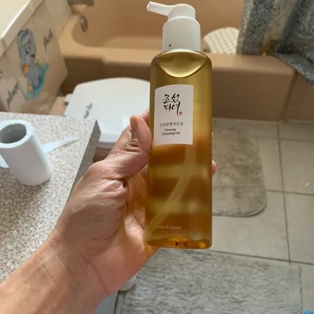 Beauty of Joseon Ginseng Cleansing Oil tenu en main dans une salle de bain, avec son flacon pompe visible.