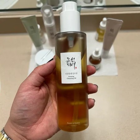 Beauty of Joseon Ginseng Cleansing Oil tenu en main devant plusieurs produits de soin dans une salle de bain.