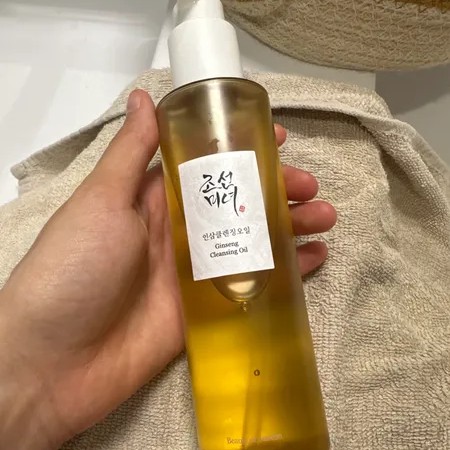Beauty of Joseon Ginseng Cleansing Oil tenu en main au-dessus d’une serviette beige près d’un lavabo.