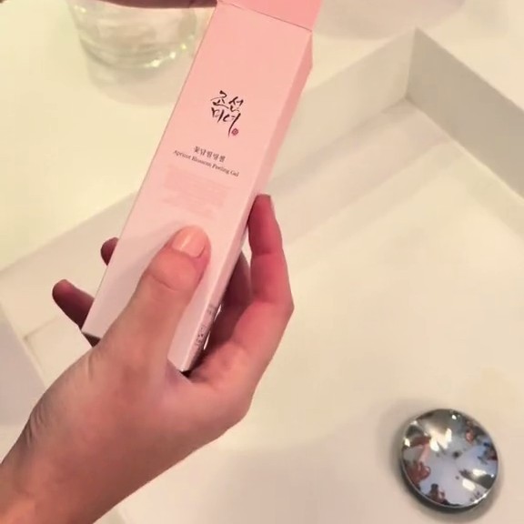 Boîte du Beauty of Joseon Apricot Blossom Peeling Gel tenue en main au-dessus d’un lavabo.