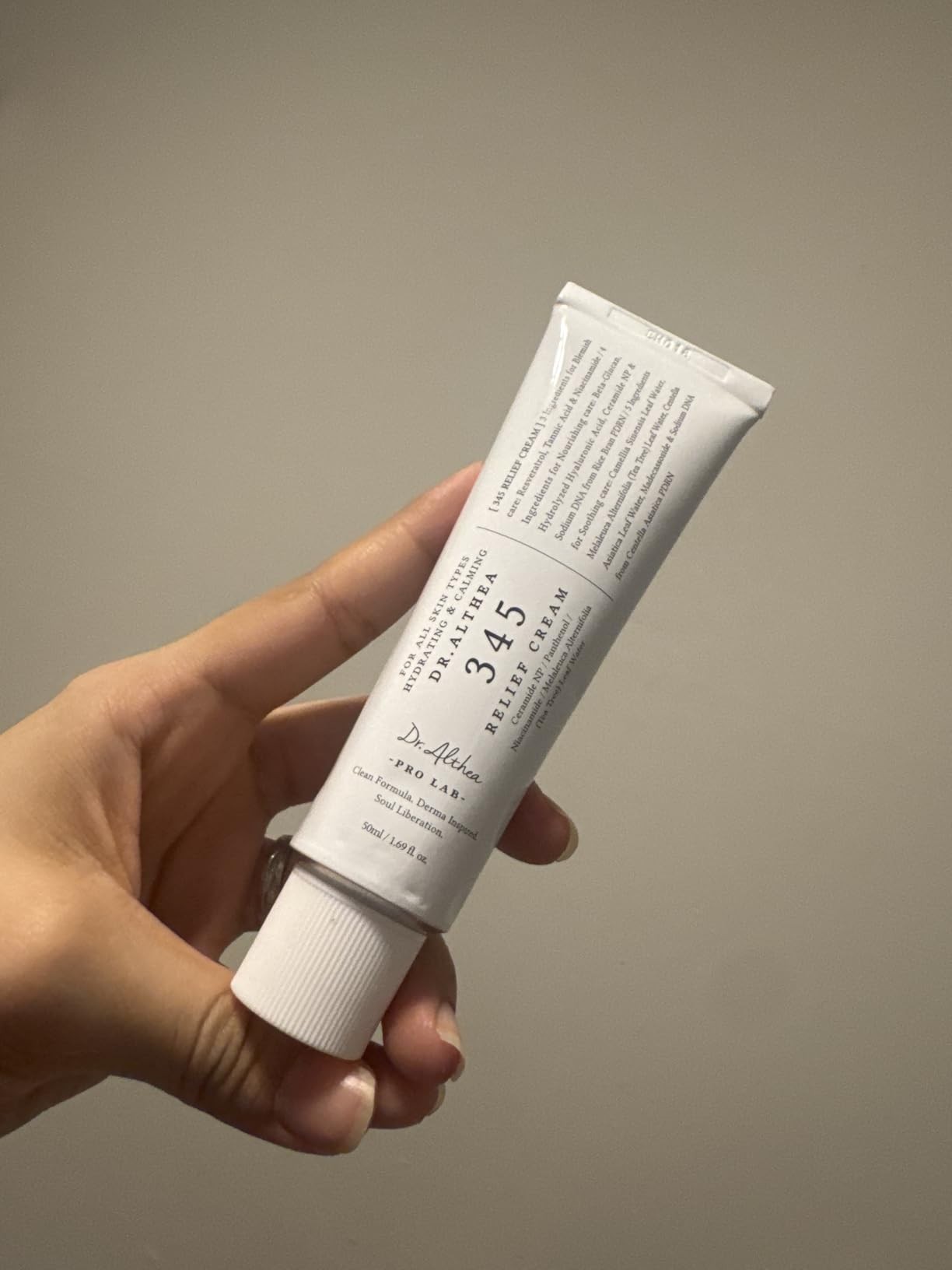 Dr. Althea 345 Relief Cream tenue en main sur fond beige, avec le packaging du produit visible.