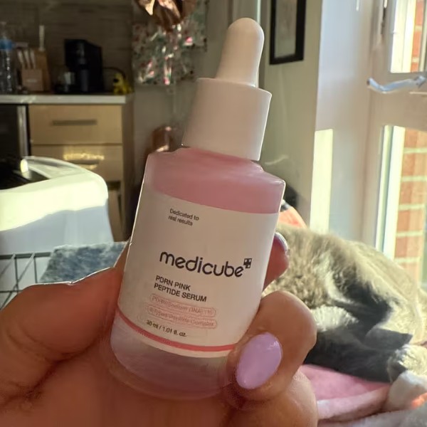 Flacon de Medicube PDRN Pink Peptide Serum tenu en main dans un intérieur lumineux