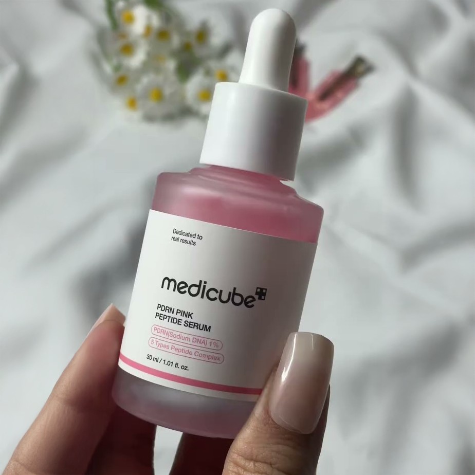 Flacon de Medicube PDRN Pink Peptide Serum tenu en main sur fond clair et fleuri