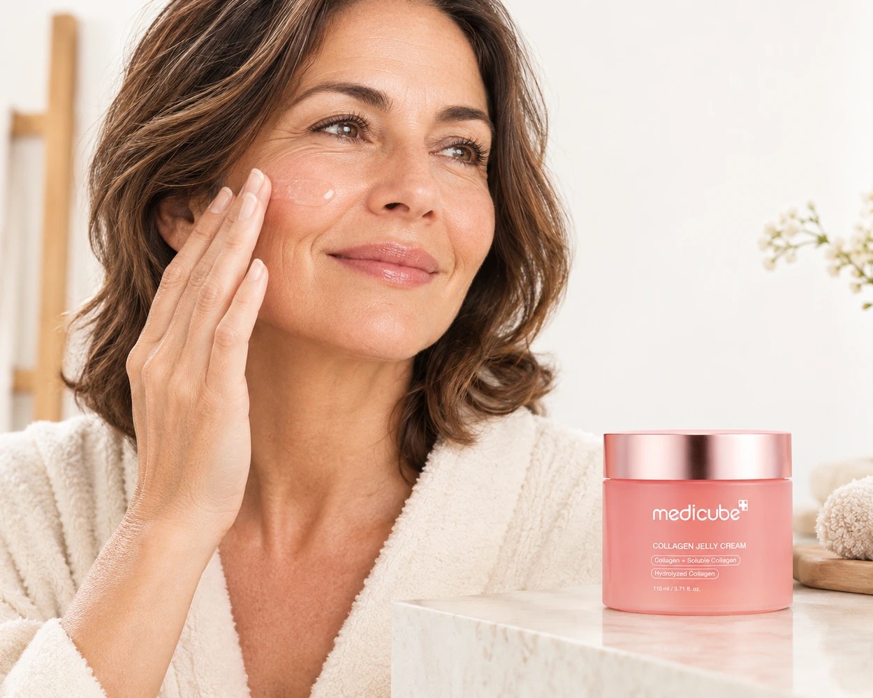 Femme à la peau mature touchant sa joue près d’un pot de Medicube Collagen Jelly Cream