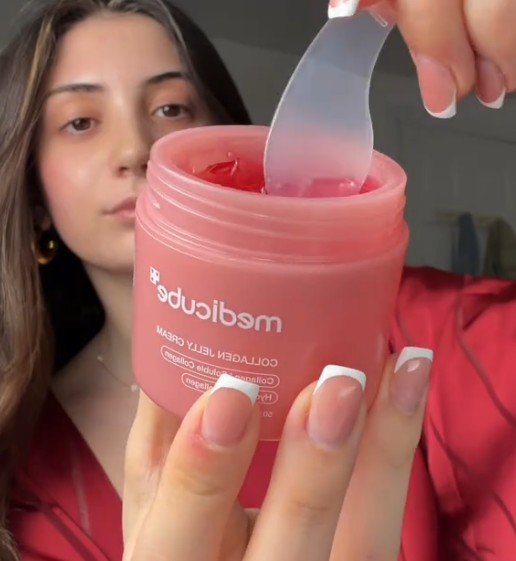 Utilisatrice tenant le pot ouvert de Medicube Collagen Jelly Cream et prélevant la gelée rose avec une spatule