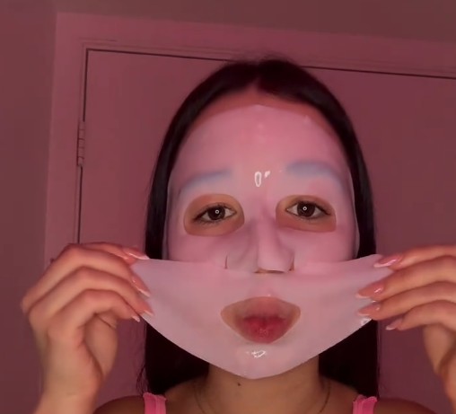Femme appliquant la partie inférieure d’un masque hydrogel rose sur le visage.