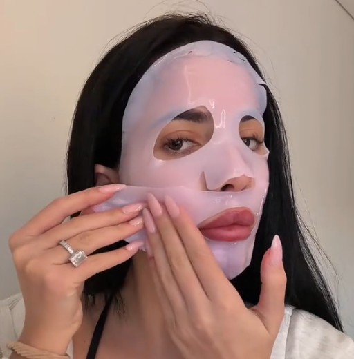 Femme lissant le masque hydrogel rose sur sa joue pour bien l’ajuster.