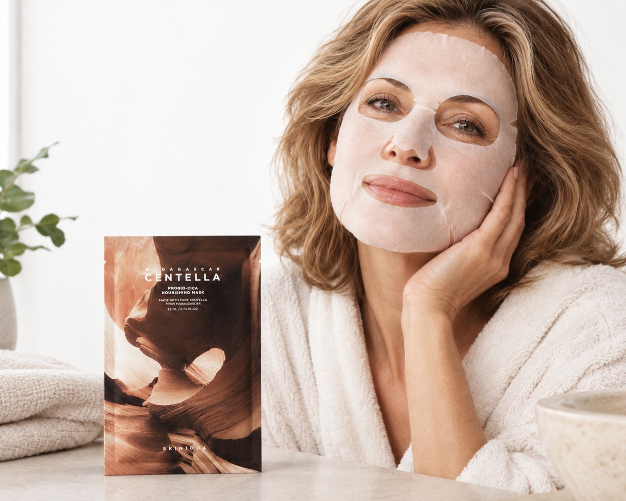 Femme portant le masque tissu SKIN1004 Probio-Cica près de son sachet dans une salle de bain claire