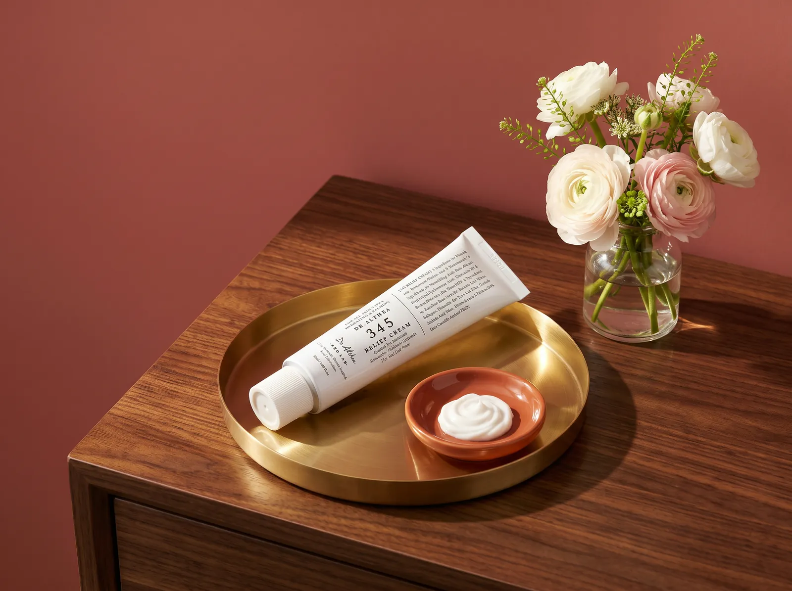 Tube de 345 Relief Cream de Dr. Althea sur un plateau en laiton, avec une coupelle de crème